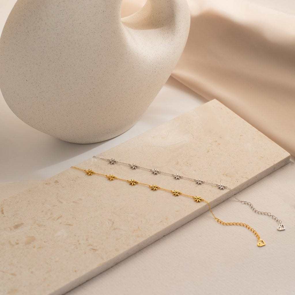 The Flower Child Bracelet, available in gold or silver, rests on a beige stone next to a ceramic vase, radiating boho-hippie charm and adding cottage-core elegance to any look.