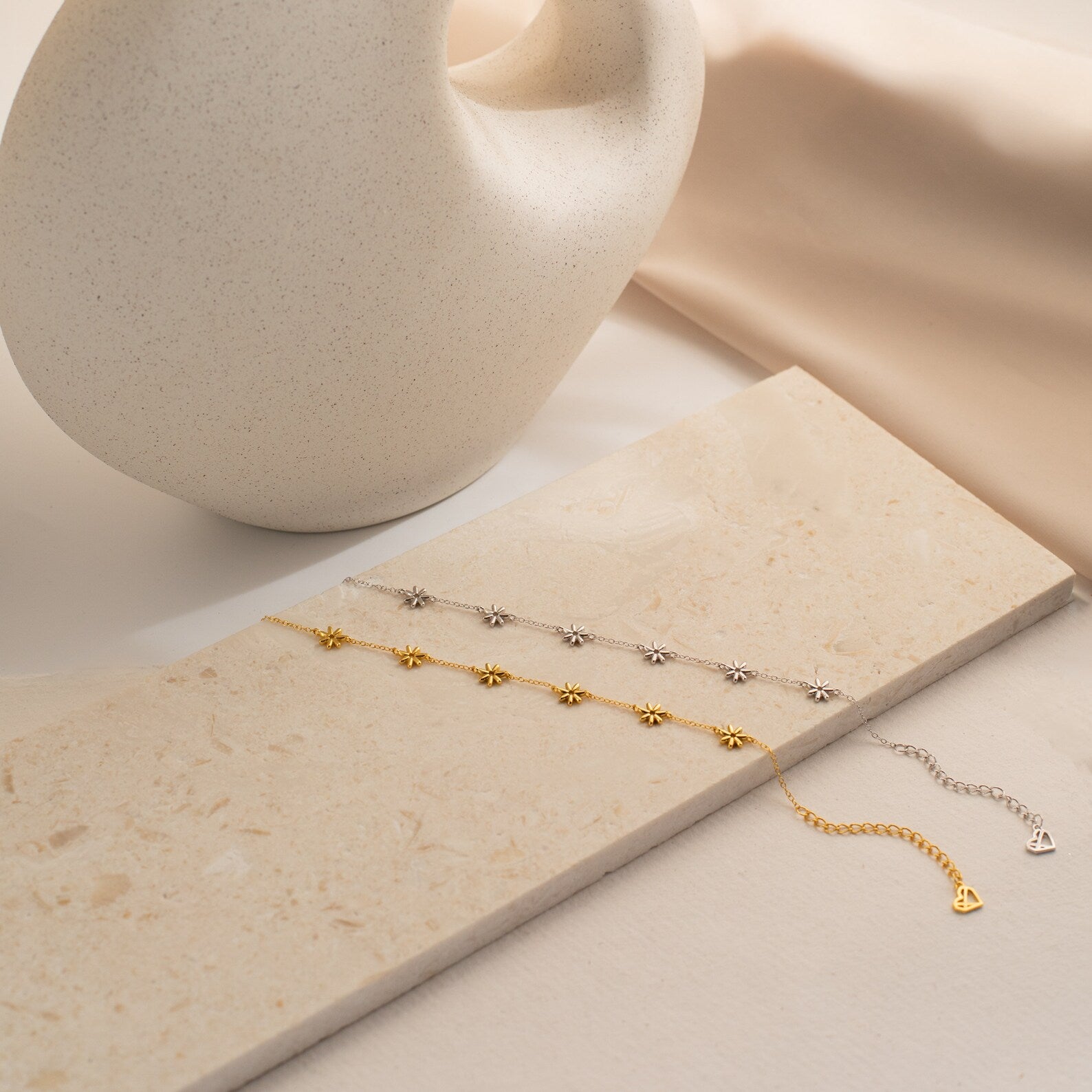 The Flower Child Bracelet, available in gold or silver, rests on a beige stone next to a ceramic vase, radiating boho-hippie charm and adding cottage-core elegance to any look.