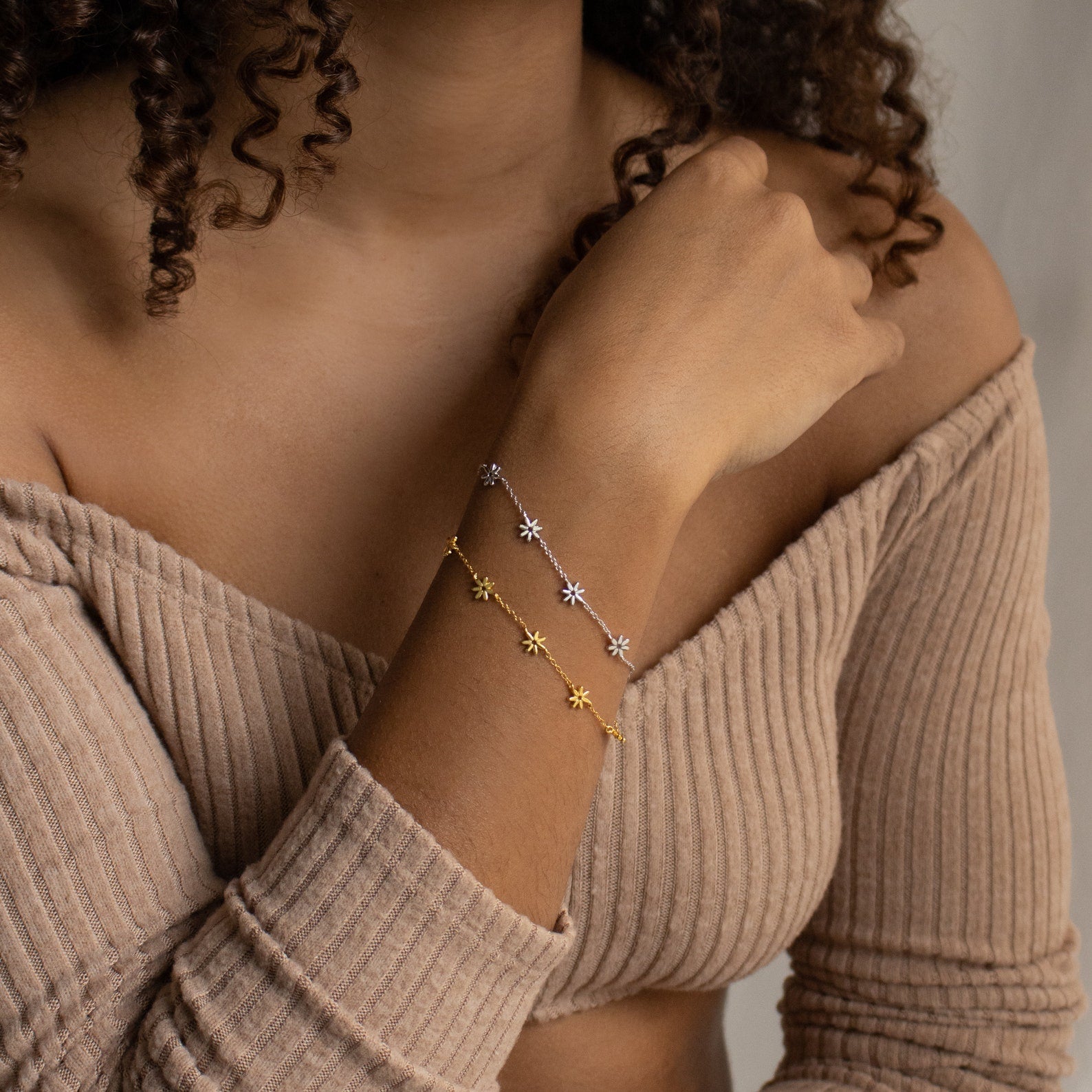 Woman wearing an off-shoulder ribbed sweater and two star-shaped charm bracelets, including the Flower Child Bracelet, on her wrist.