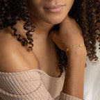 A woman with curly hair wears an off-shoulder top and the Flower Child Bracelet, a delicate, boho-hippie accessory adorned with star-shaped charms.