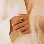 A person wearing the Black Signet Ring—a unisex gold band with a black stone—paired with cream-colored, textured clothing.