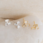 Glacier Diamond Studs come in two pairs—one silver, one gold—each with three clear, baguette-shaped stones, offering a modern update on classic stud earrings.