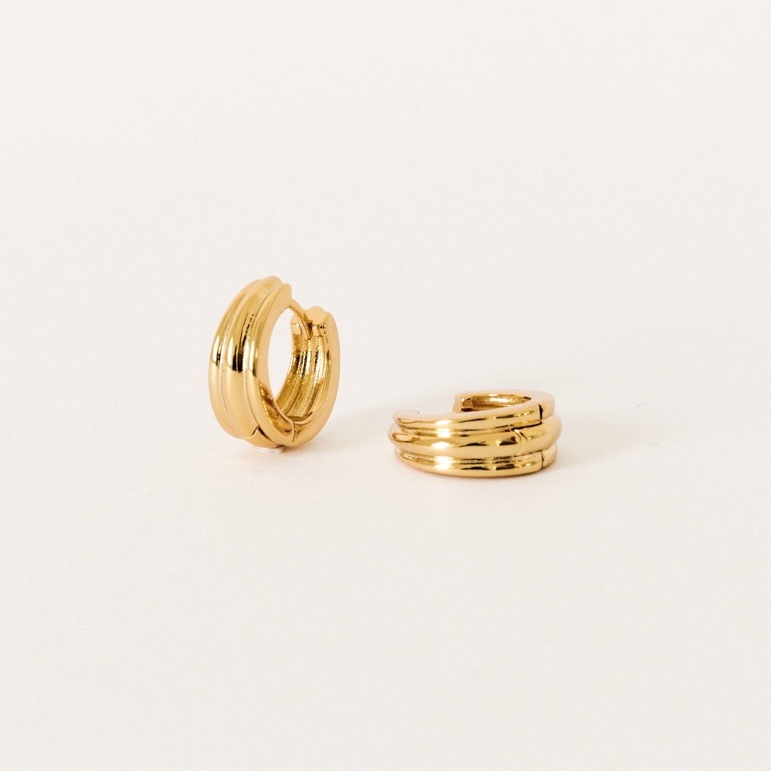 The Canal Chunky Hoops are small gold triple-band huggie earrings with a modern design, ideal for everyday wear. Shown on a plain white background.