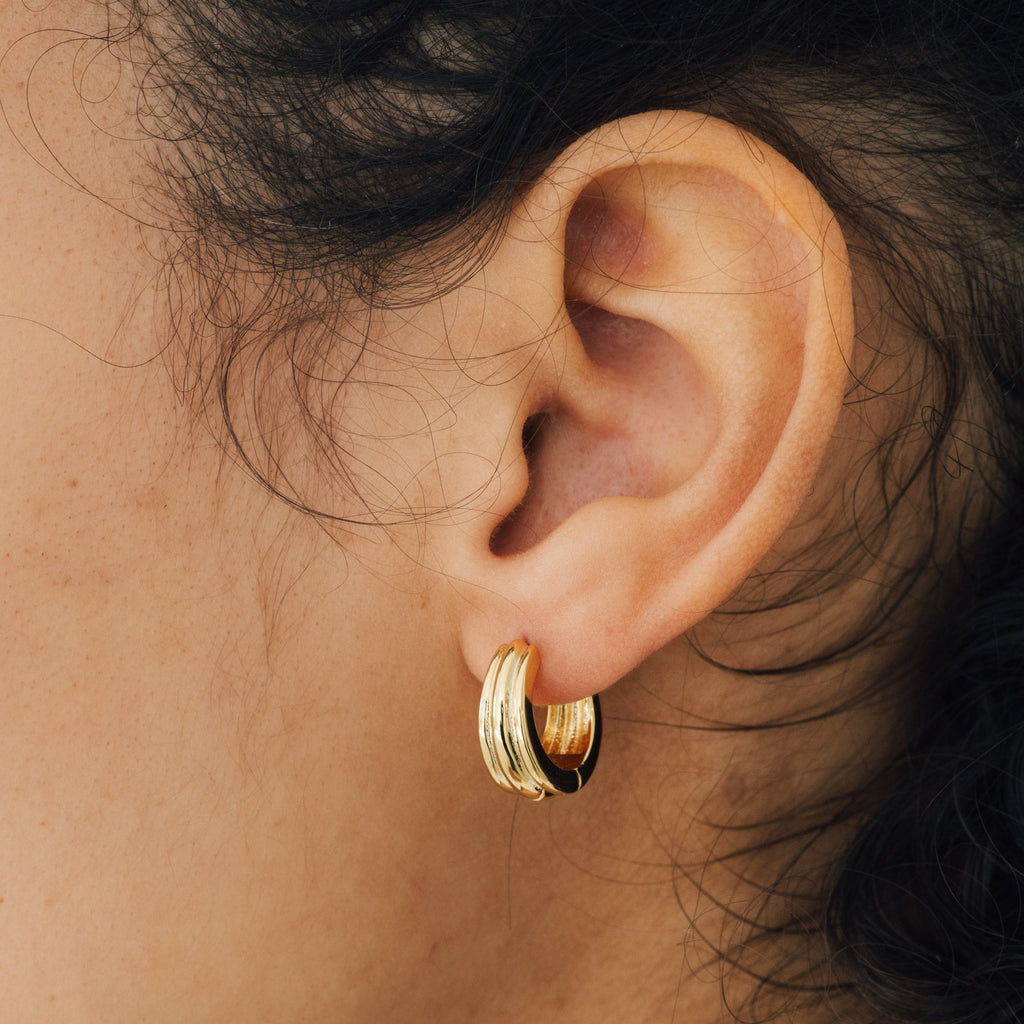Close-up of a person’s ear wearing Canal Chunky Hoops—small, thick gold earrings with wavy details—perfect contemporary huggies for everyday wear.