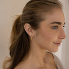 A woman with light brown hair in a ponytail, smiling softly and looking to the right, wears the Amia Pave Link Earrings.