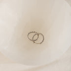 Two Aster Pave Twisted Hoops, crafted in silver and elegantly intertwined, are displayed inside a white, translucent bowl.