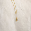 The Sage Diamond Necklace features a gold chain and a rectangular clear gemstone pendant, displayed on white fabric—an effortless touch of timeless elegance.