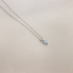 Opal Drop Necklace with a delicate silver chain and an iridescent opal teardrop pendant, shown on a light beige background.