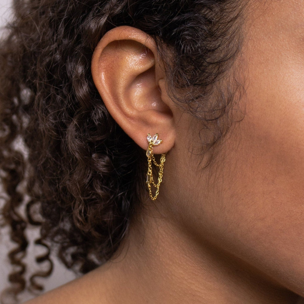 Close-up of a woman's ear with curly hair, wearing Genesis Chain Earrings: statement gold chain earrings featuring a leaf-shaped stud.