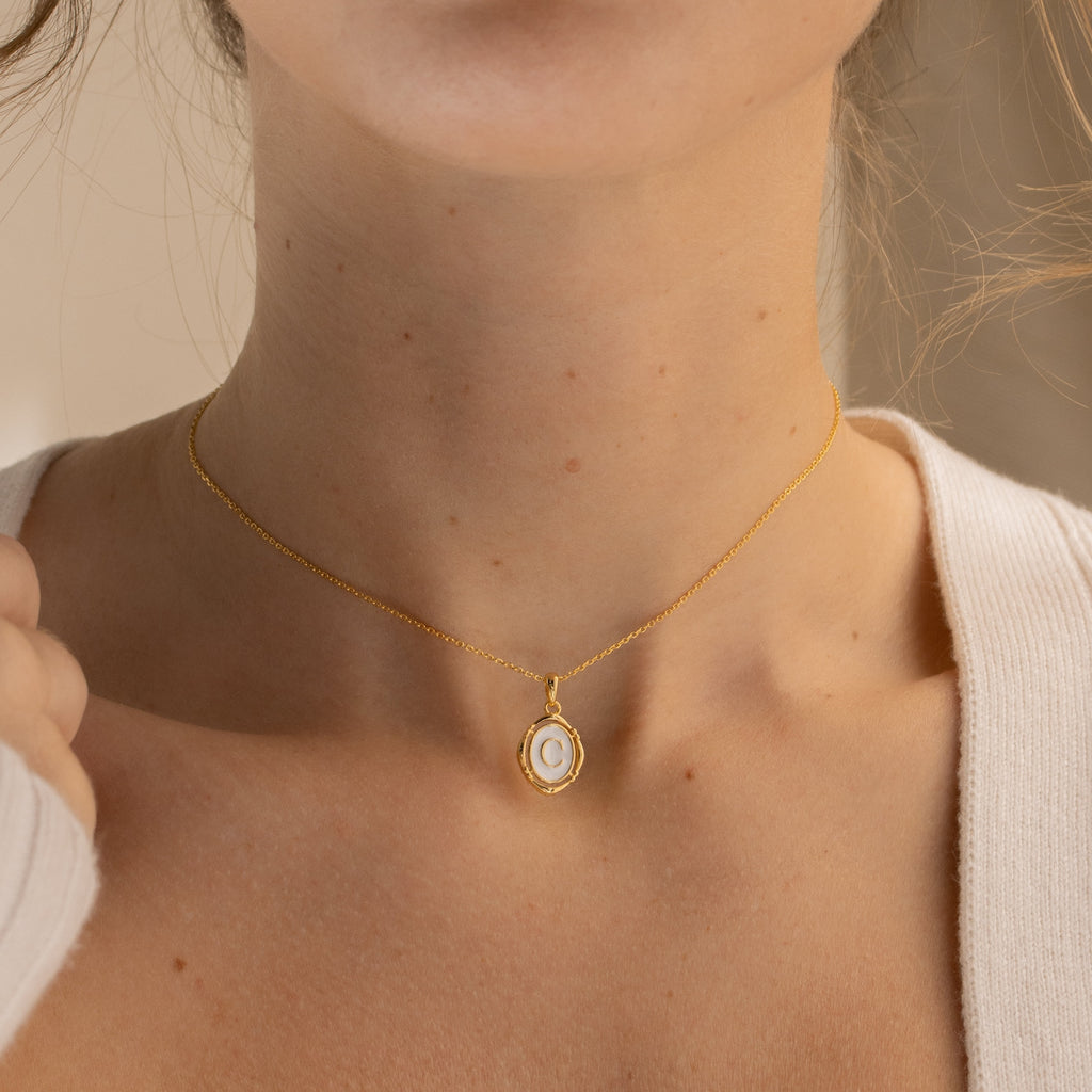 A woman wearing the Initial Pendant Necklace in 18K Gold, featuring a vintage-inspired oval enamel pendant with the letter C.