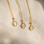 Three Initial Pendant Necklaces in 18K Gold, featuring round C, M, and K charms, are displayed on a soft beige fabric background, adding timeless vintage style to any outfit.