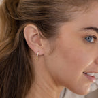 A woman with blue eyes smiles, wearing the Emily Pave Star Huggies—a small gold hoop earring with a star charm on her left ear, perfect for celestial jewelry lovers.