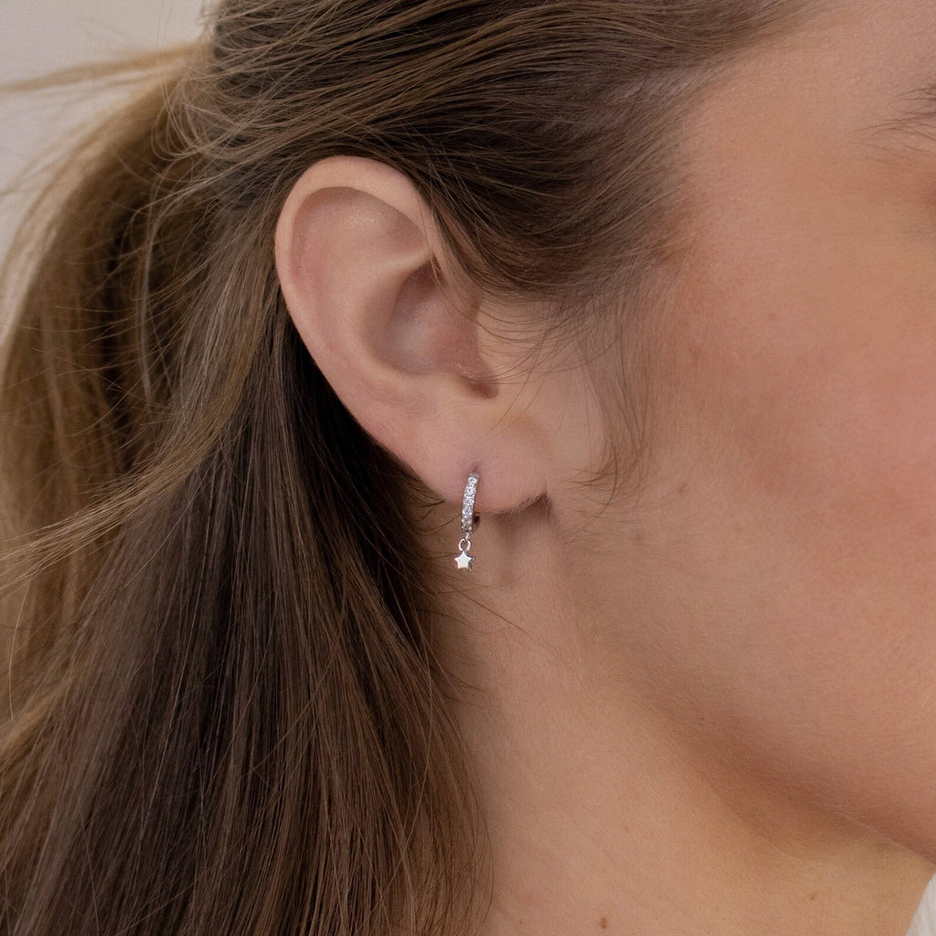 Close-up of a woman's ear wearing the Emily Pave Star Huggies, small silver earrings with a delicate dangling star charm—a subtle and celestial jewelry piece.