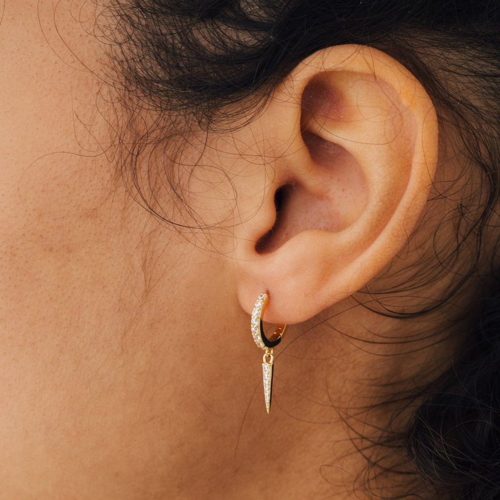 Close-up of an ear wearing Quinn Pave Dagger Huggies—edgy hoop earrings with diamond-studded, pointed pendants for a bold statement.