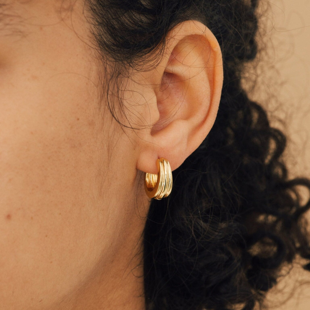 Close-up of a person’s ear with curly hair, wearing Canal Chunky Hoops—layered design earrings that are perfect for a bold, modern everyday look.
