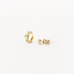 The Glacier Baguette Huggies feature gold hoops with geometric shapes and rectangular clear stones for minimalistic sparkle, elegantly shown on a white background.