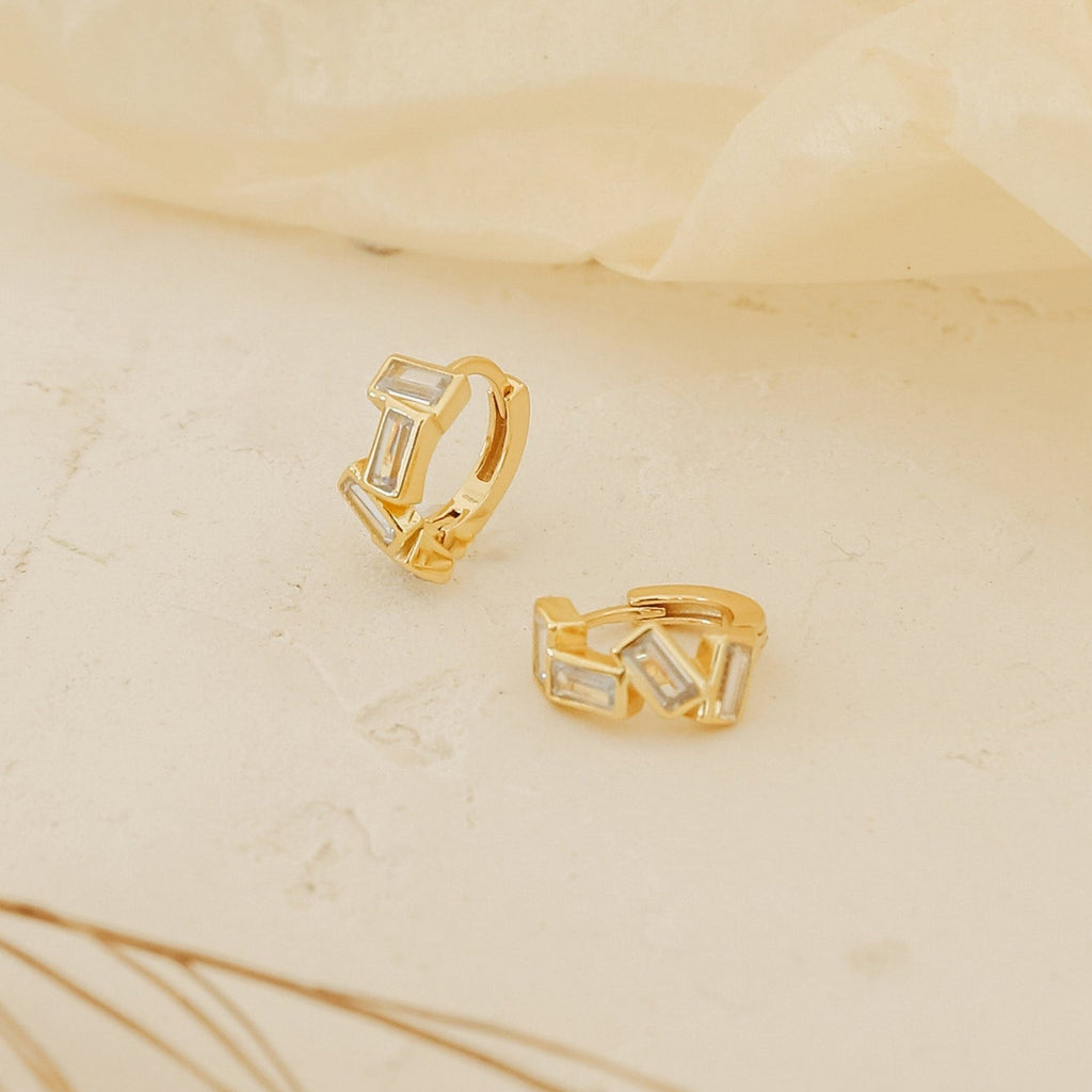 Glacier Baguette Huggies with rectangular white stones add minimalistic sparkle, shown on a light textured surface against a soft background.