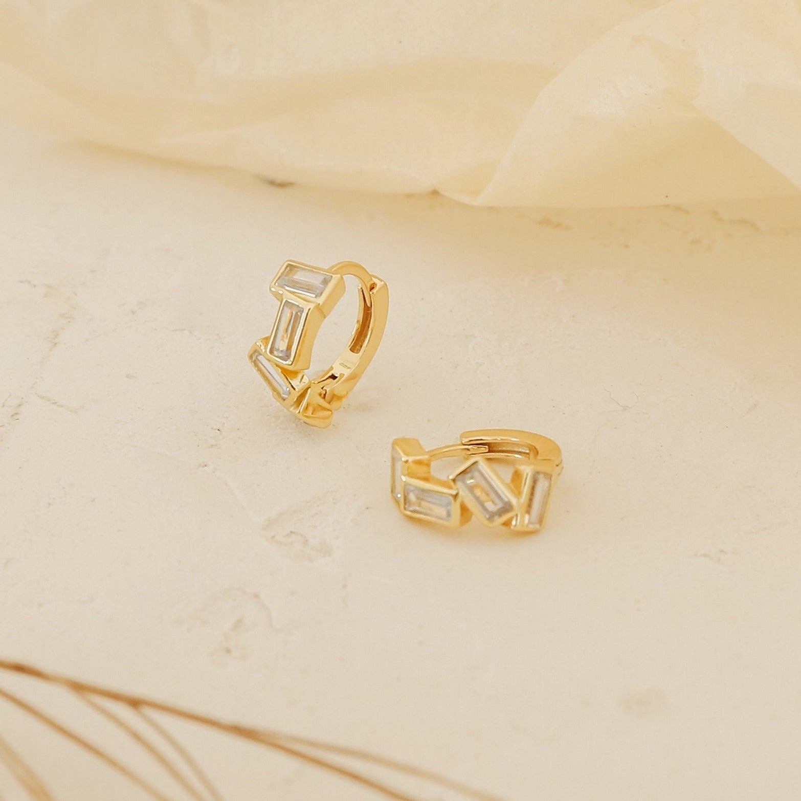 Glacier Baguette Huggies with rectangular white stones add minimalistic sparkle, shown on a light textured surface against a soft background.