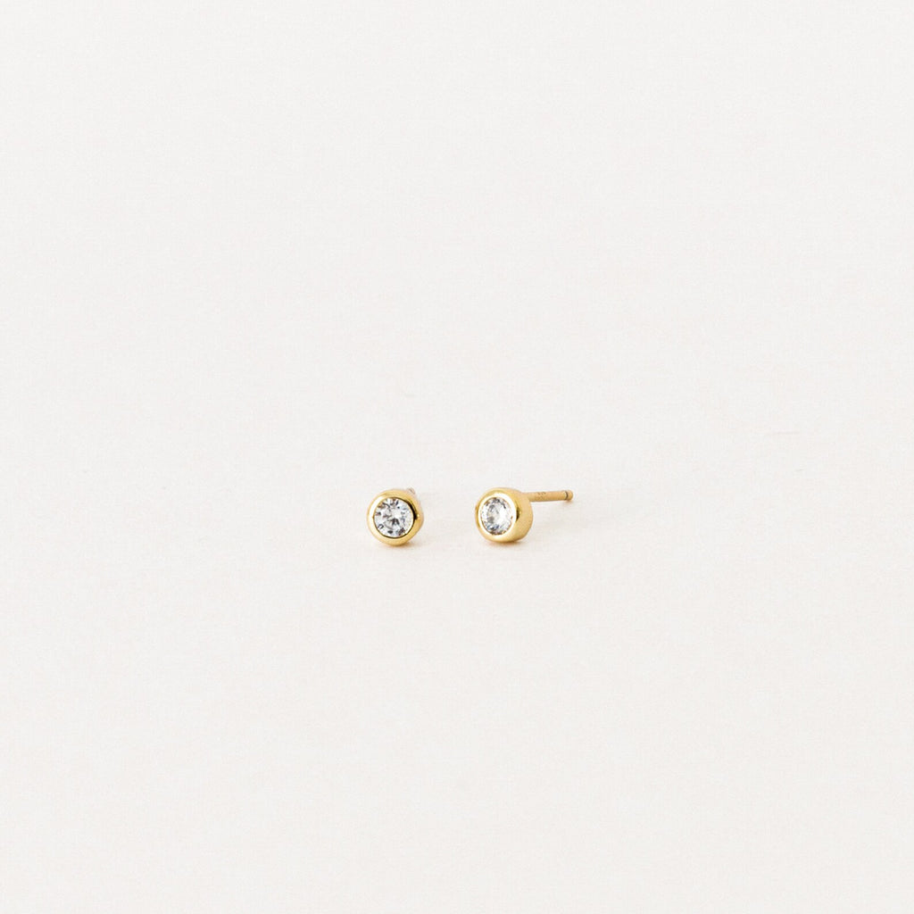 Jane Diamond Studs: small gold earrings with round brilliant diamonds, bezel set for a timeless look, displayed on a plain white background.