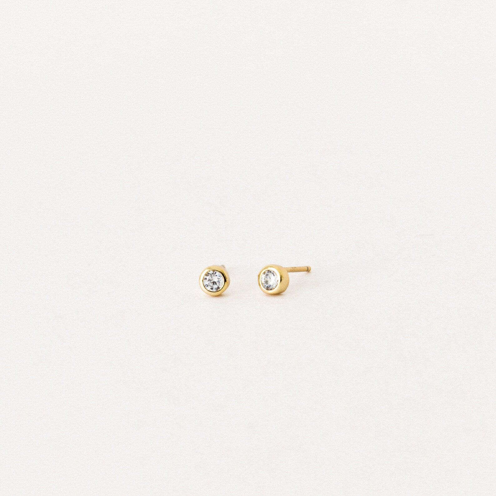 Jane Diamond Studs: small gold earrings with round brilliant diamonds, bezel set for a timeless look, displayed on a plain white background.