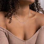 A woman showcases the Monet Duo Chain—two delicate silver necklaces, a snake and a Singapore chain—styled with an off-shoulder ribbed beige top that highlights her collarbones.