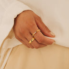 A hand wearing the Rainbow Crystal Ring, featuring pastel toned gemstones, rests on light beige fabric; nails painted nude.