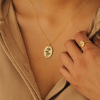 The Oval Flower Necklace features a unique flower pendant worn on the neck, perfectly complemented by a matching gold ring.