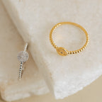 The Eden Sun Ring, featuring a radiant sunburst design and beaded band in silver, exudes boho-chic charm as it rests stylishly on a white stone surface.