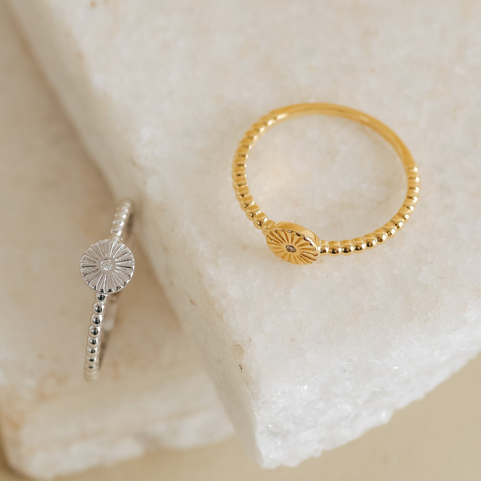 The Eden Sun Ring, featuring a radiant sunburst design and beaded band in silver, exudes boho-chic charm as it rests stylishly on a white stone surface.
