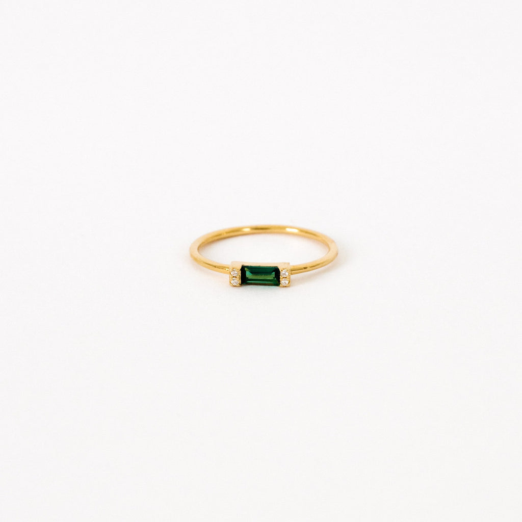 The Empire Emerald Ring features a rectangular emerald center flanked by small clear stones on a classic gold band, shown on a white background.
