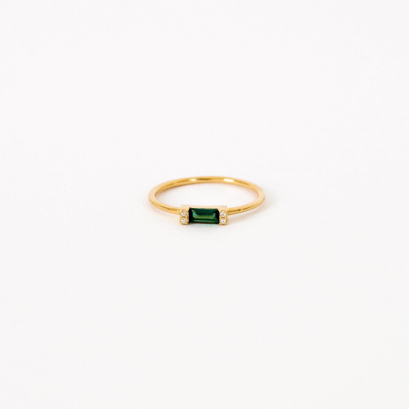The Empire Emerald Ring features a rectangular emerald center flanked by small clear stones on a classic gold band, shown on a white background.