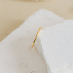 The Juliet Diamond Ring is a delicate piece, showcasing a slim gold band with sparkling diamonds, beautifully displayed on a white textured stone.