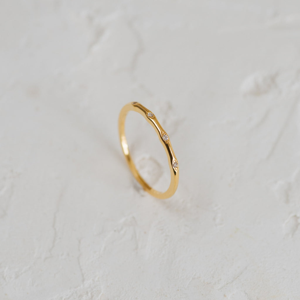 The Juliet Diamond Ring, a minimalist piece with three small diamonds, shines elegantly on a white textured surface.