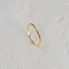 The Juliet Diamond Ring, a minimalist piece with three small diamonds, shines elegantly on a white textured surface.