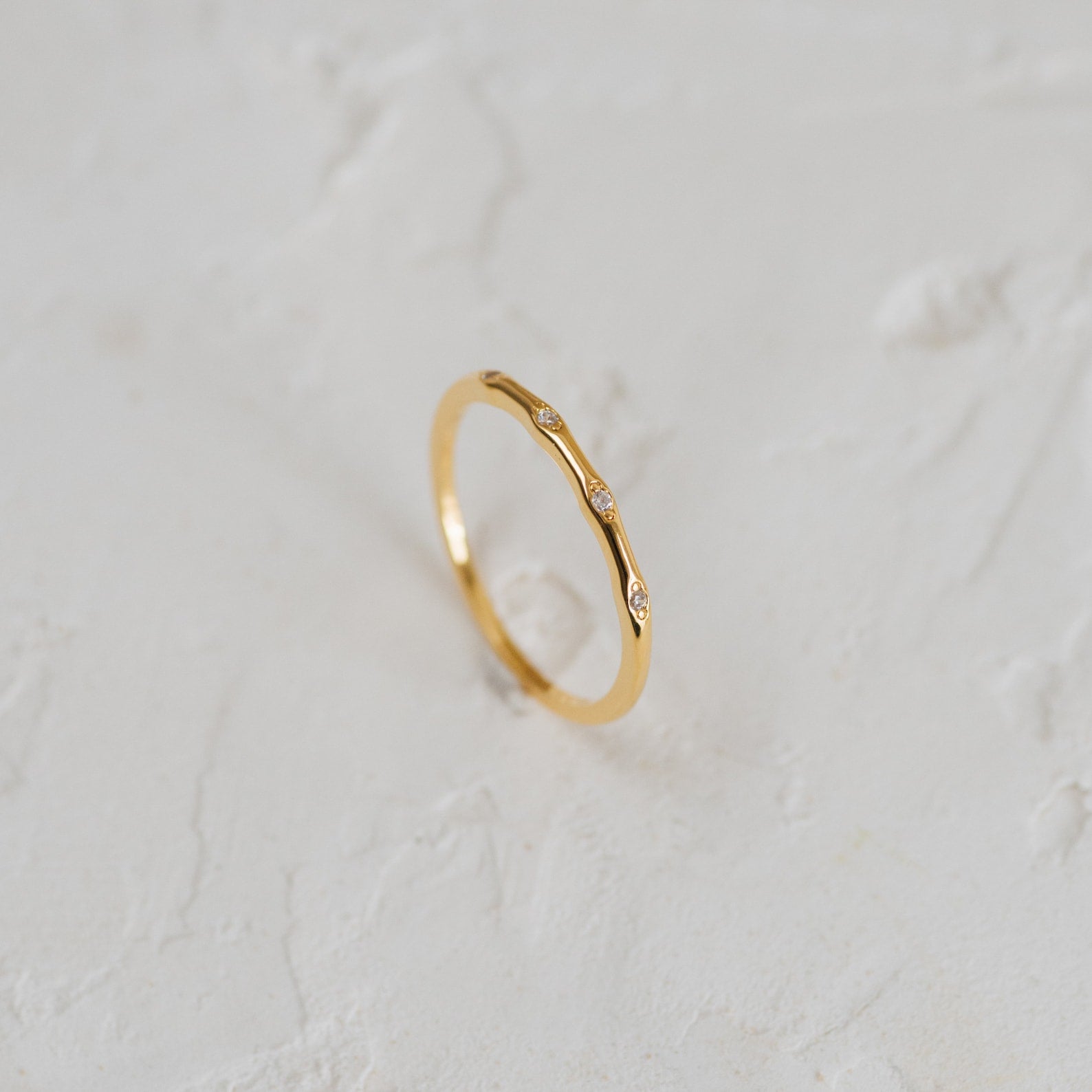 The Juliet Diamond Ring, a minimalist piece with three small diamonds, shines elegantly on a white textured surface.
