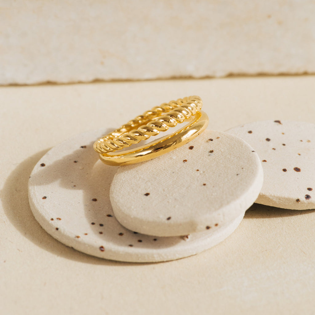Flat lay of Chelsea Duo Ring in gold with rope and smooth band detail placed on speckled stone props.