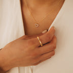 A woman wears the Forever Pave Heart Necklace and a gold ring with small stones, holding her shirt collar.