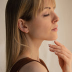 Woman with long blonde hair, eyes closed, and soft makeup poses in profile with hand near chin, wearing the Booker Tiny Diamond Studs as her go-to everyday earrings.