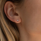 Close-up of a woman's ear wearing Booker Tiny Diamond Studs, minimal diamond earrings perfect for everyday wear, with light brown hair visible.