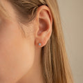 Close-up of a womans ear with straight blonde hair, wearing Booker Large Diamond Studs—minimalist sterling silver earrings. The neutral background is out of focus.