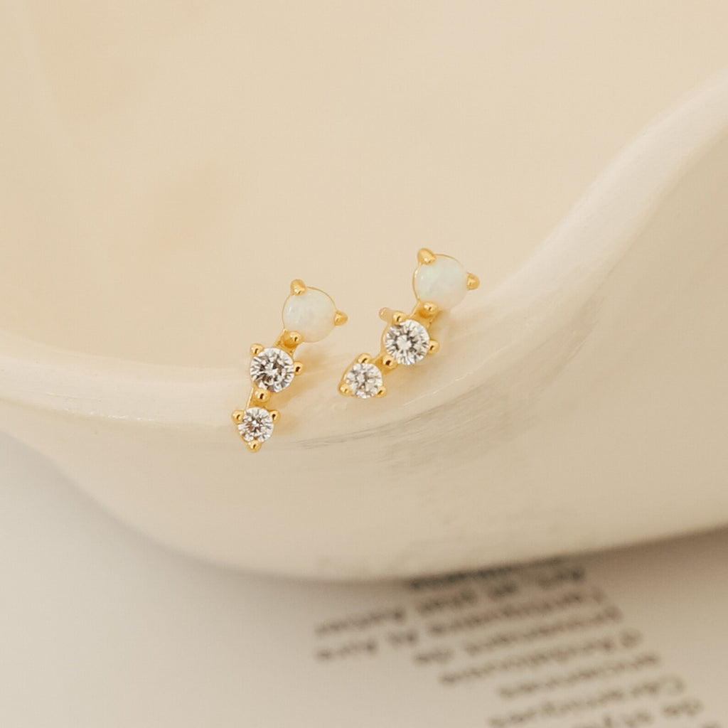 Maeve Opal Studs: Gold statement earrings accented with two white stones and two clear crystals per earring, displayed on a cream ceramic dish.