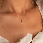 Gold necklace featuring a rectangular emerald-cut crystal pendant, worn by a model in a white ruffled top, highlighting the clean, geometric lines and radiant clarity of the stone.