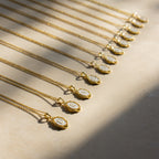 Initial Pendant Necklace, featuring a gold enamel finish and vintage-inspired design, is elegantly arranged in a row on a light surface and shimmers beautifully in sunlight.