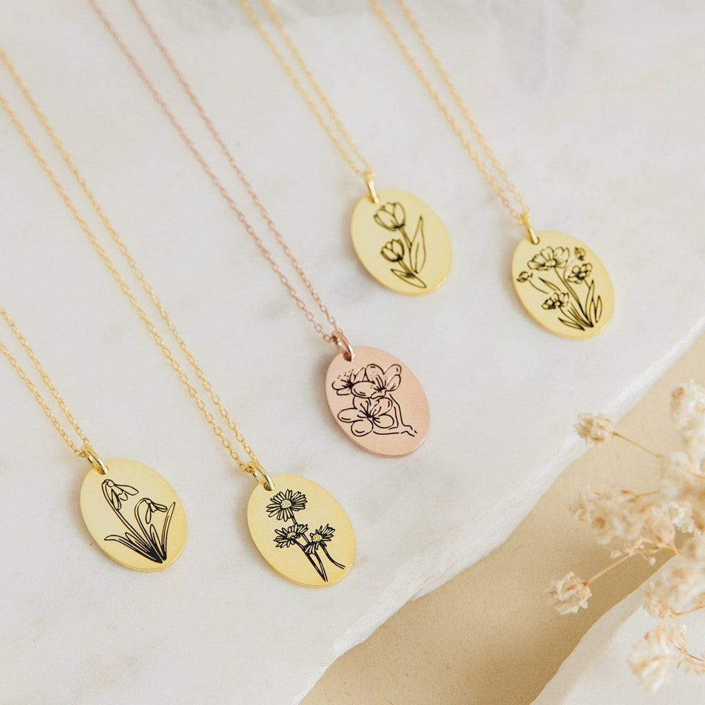Five Oval Flower Necklaces in Rose Gold with engraved floral designs displayed on marble—a beautiful personalized gift for her.