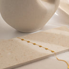 The Flower Child Bracelet, a delicate gold piece with star-shaped charms, displayed on beige stone near a ceramic vase, brings a cottage-core touch to your style.