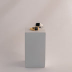 Two Black Signet Rings—square, unisex, one with gold and one with silver accents—are displayed on a minimalist gray block. These bold statement rings suit any style.