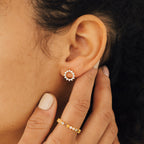 Close-up of a woman's ear adorned with Helen Diamond Sun Studs; her hand with a gold ring gently touches her ear.