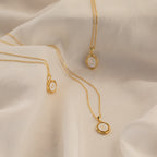 Three Initial Pendant Necklaces in 18K Gold, each featuring a round charm engraved with a C, M, or K, are displayed on soft fabric.