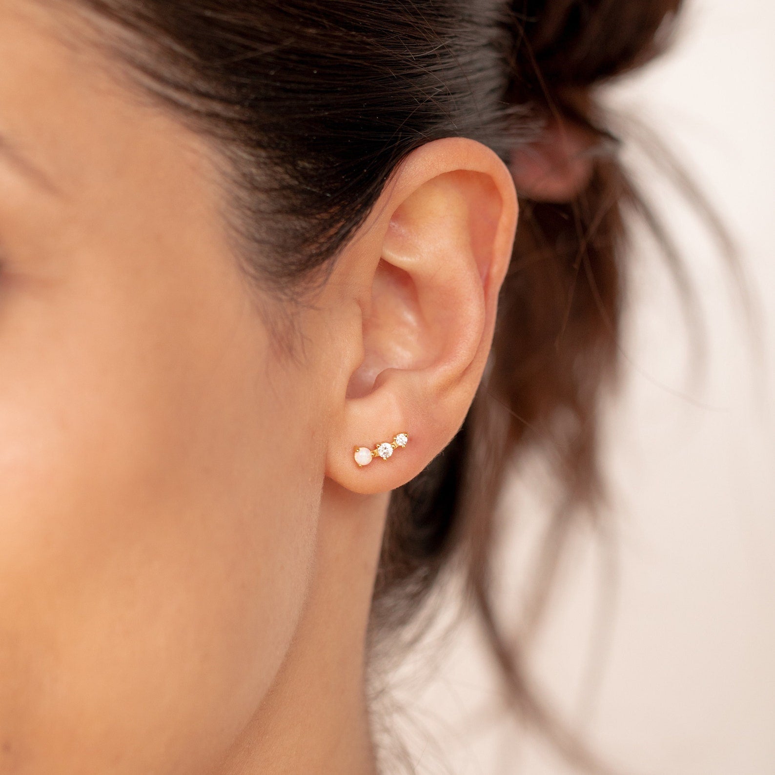 Close-up of a woman's ear wearing two small gemstone earrings—one gold stud and one clear stone—ideal for mixing with Maeve Opal Studs or pairing with other statement pieces.