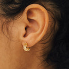 Close-up of an ear wearing a small, gold, wavy Maze Half Hoop earring—perfect for your unique stack. The blurred background draws attention to these elegant hoops.
